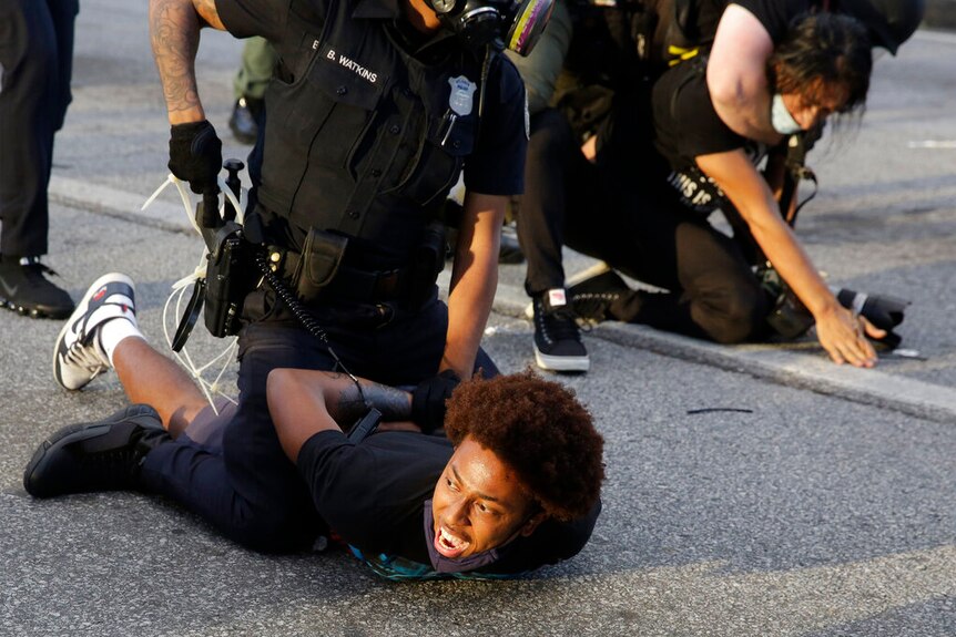 Demonstrators held on the ground by police.