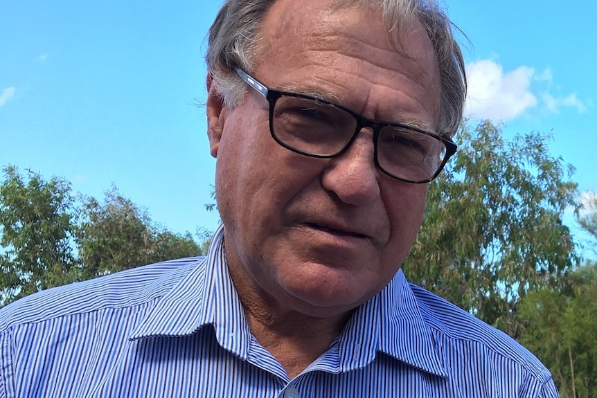 A man in a blue shirt and glasses looks at the camera