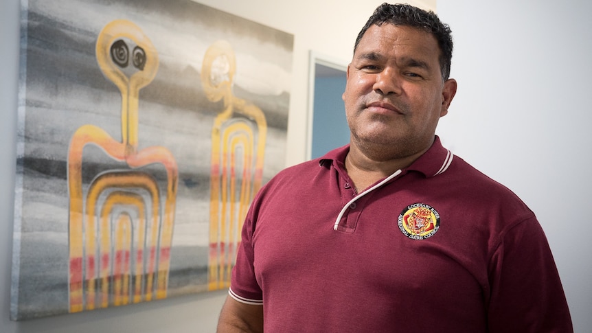 Councillor Wayne Butcher, mayor of the Lockhart River Aboriginal Shire Council, stands in front of a Fiona Omeenyo artwork.