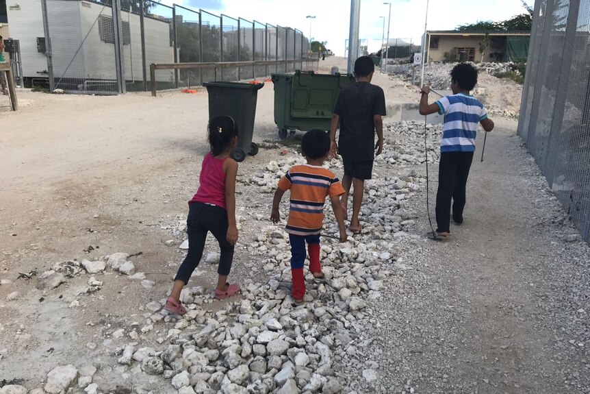 Four children walk past a fence.