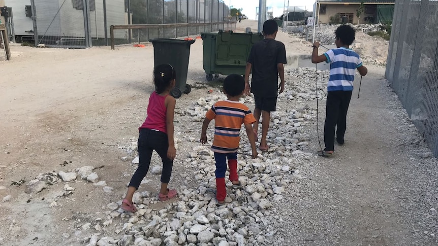 Four children walk past a fence.