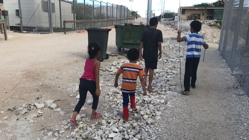 Four children walk past a fence.