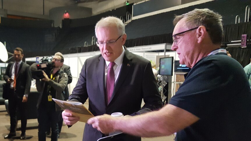 A man hands Prime Minister Scott Morrison a paper report