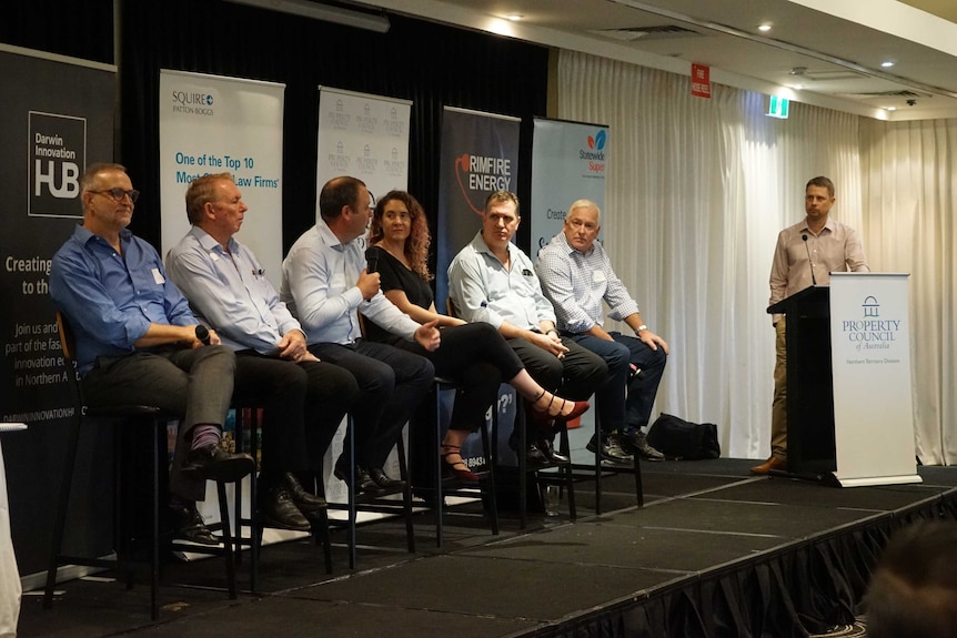 Cris Cureton is wearing a blue shirt and sitting on a panel with four other men and one woman.