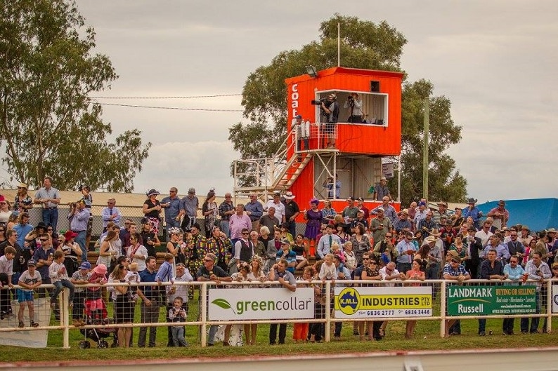 A big crowd stand under the tower and along the fence at Cobar track.