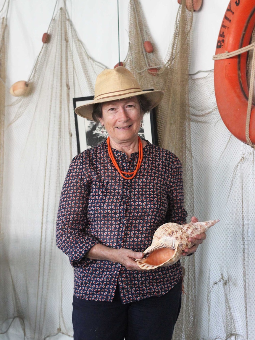 A woman holds a large shell.