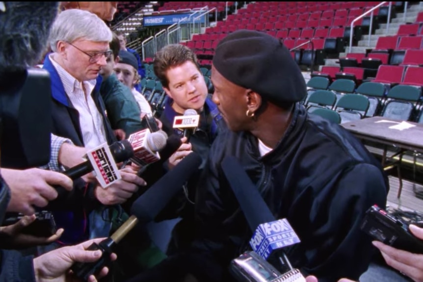Michael Jordan wears a beret while reporters ask him questions.