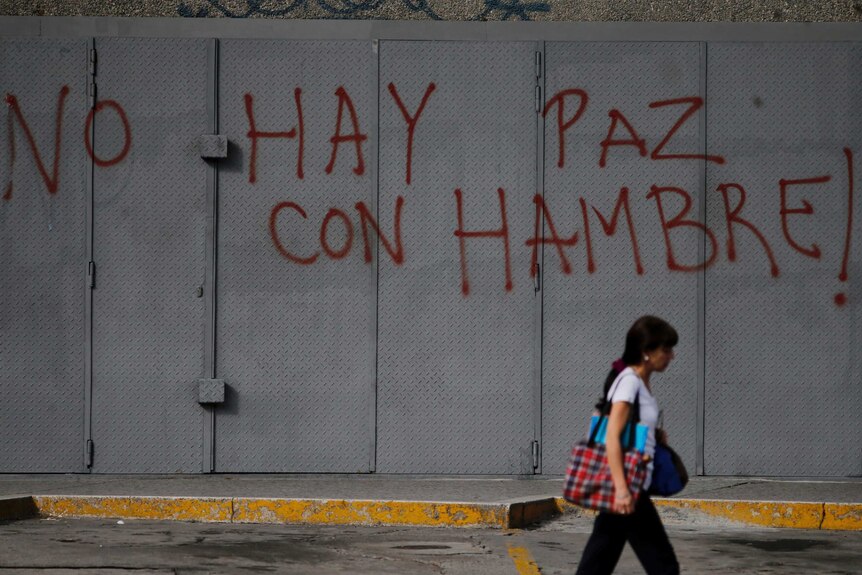 Woman walks past 'There is no peace with hunger' graffiti in Venezuela