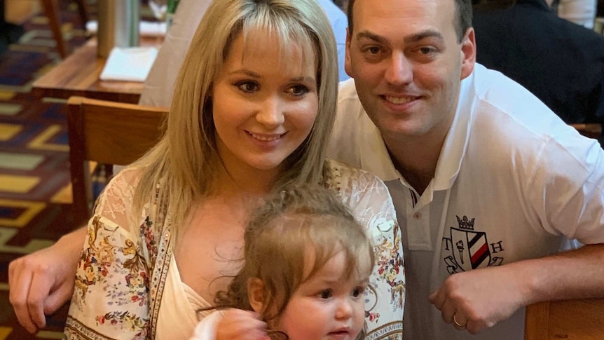 A woman holding a young girl sits with a man who has his arm around her.