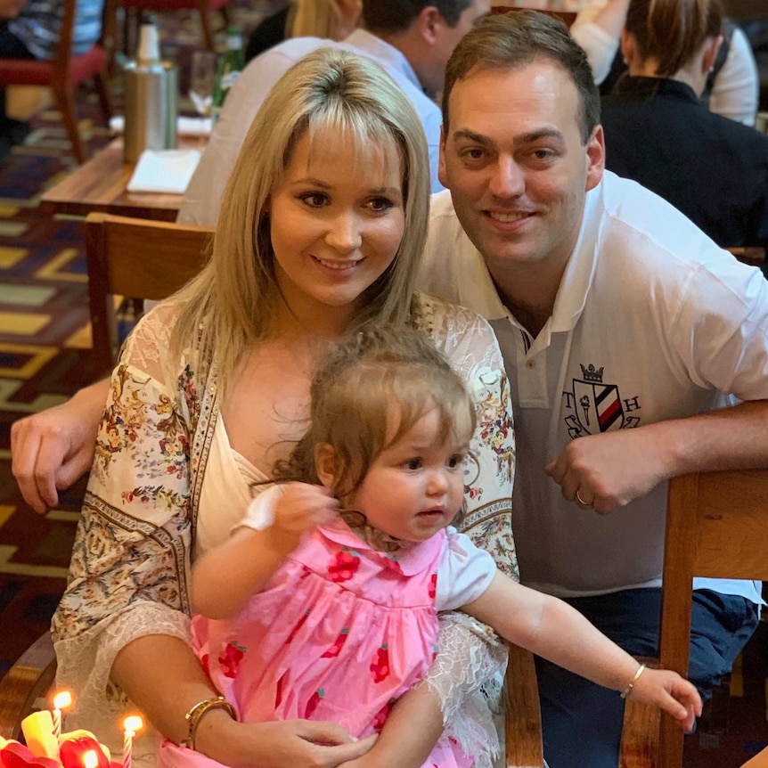 A woman holding a young girl sits with a man who has his arm around her.