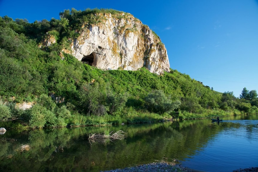 A rocky hill rises over water and trees