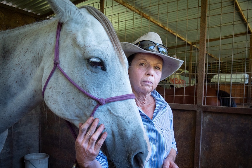 A portrait of a woman wearing a large hat standing behind the head of a white horse.