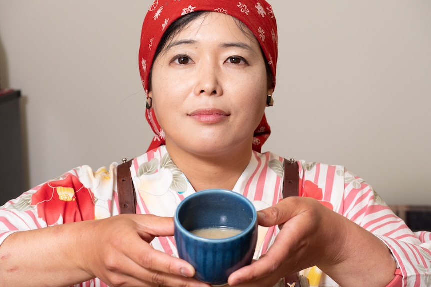 Woman wearing traditional Japanese clothing holding cup of miso soup