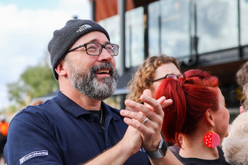 A man with a beanie and glasses cries and smiles with joy