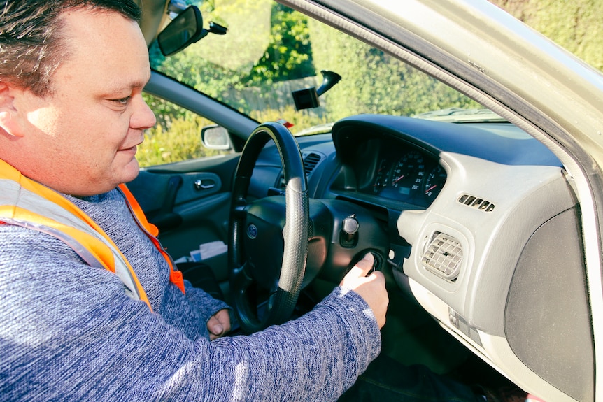 A man in a high-vis vest turns the key in the ignition of his car.