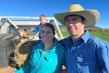 A man in a hat stands beside a woman in a green shirt.