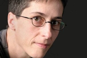 A close-up photo of Alison Bechdel with short dark hair, glasses and closed-mouth smile.