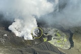 An aerial photo shows the grey-black vent of Whakaari-White Island spewing white gas from its mouth.