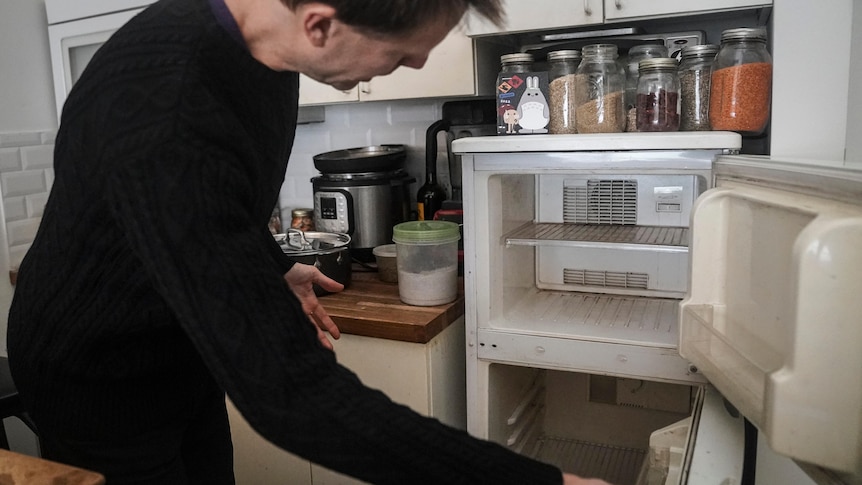 a man in a black shirt opens up an empty refrigerator in a kitchen