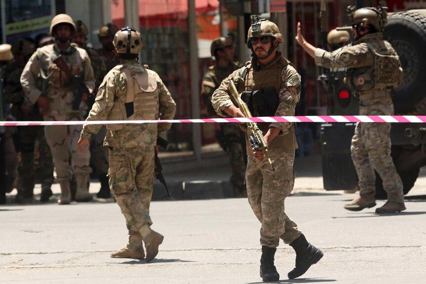 Afghan military official point gun down behind warning tap, surrounded by other officers