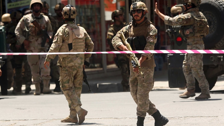 Afghan military official point gun down behind warning tap, surrounded by other officers
