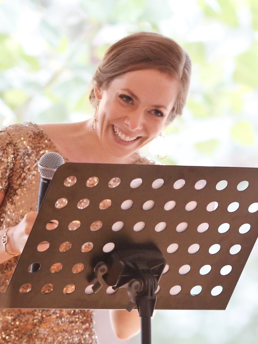 A woman in a gold sparkly gown laughs while standing at a lectern with a microphone