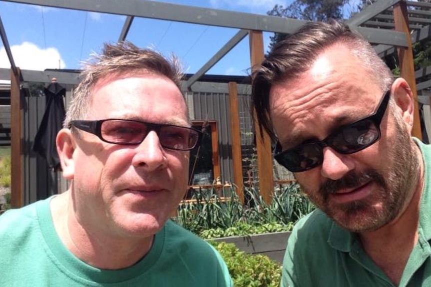 A picture of two men in a harden, one wearing sunglasses and the other glasses and both wearing green shirts.