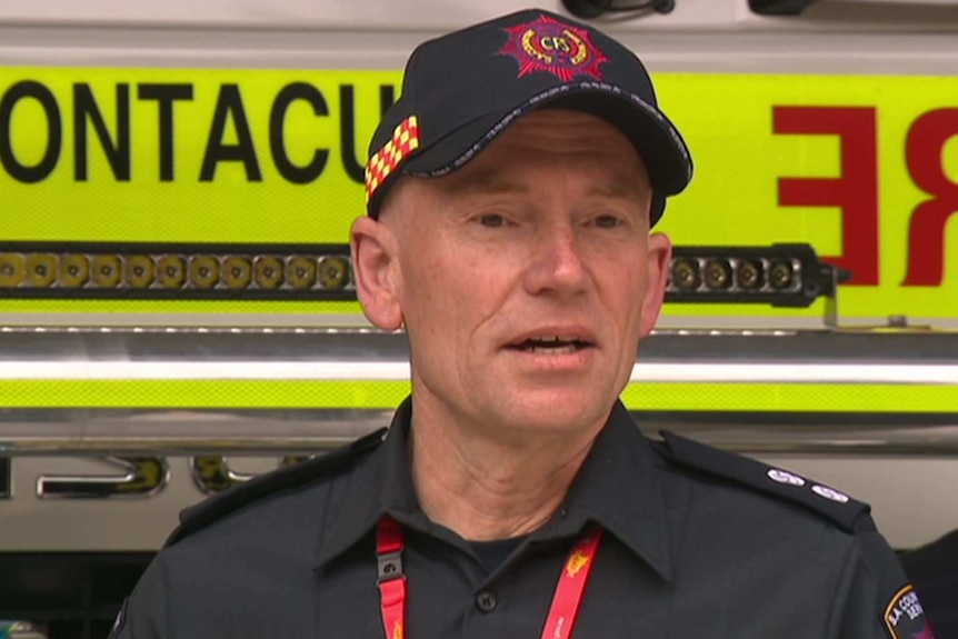 A man in a CFS hat and uniform in front of a fire truck (centre) with another man in a collared shirt.