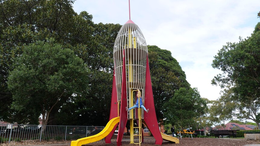 A young girl hangs off play equipment in the shape of a rocket