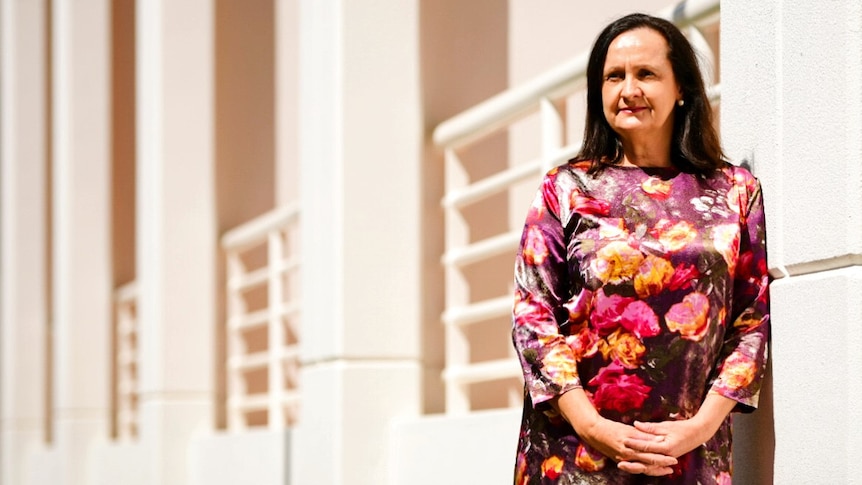 Robyn Lambley is wearing a long sleeved floral dress and is outside Parliament House with a serious expression.