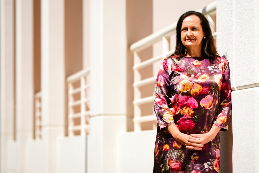 Robyn Lambley is wearing a long sleeved floral dress and is outside Parliament House with a serious expression.