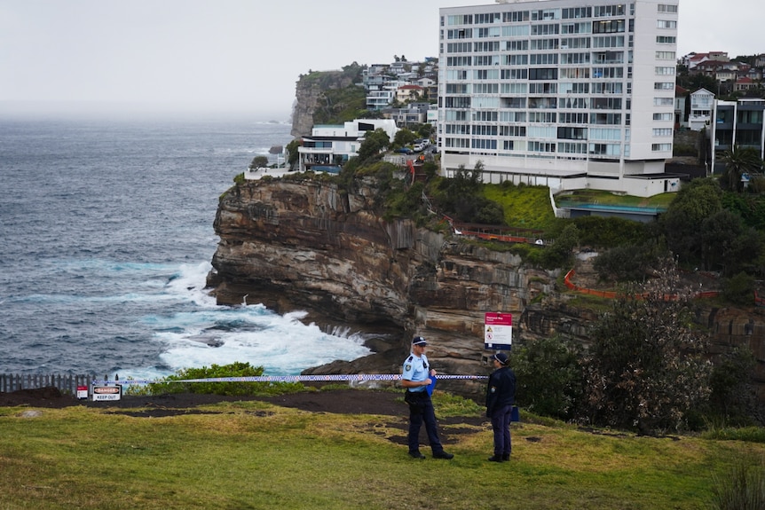 Police officers at Diamond Bay Reserve clifftop in Vaucluse with police tape behind them. Ocean and apratrtment block behind