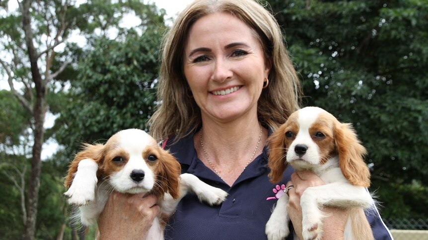 A smiling woman holds two puppies