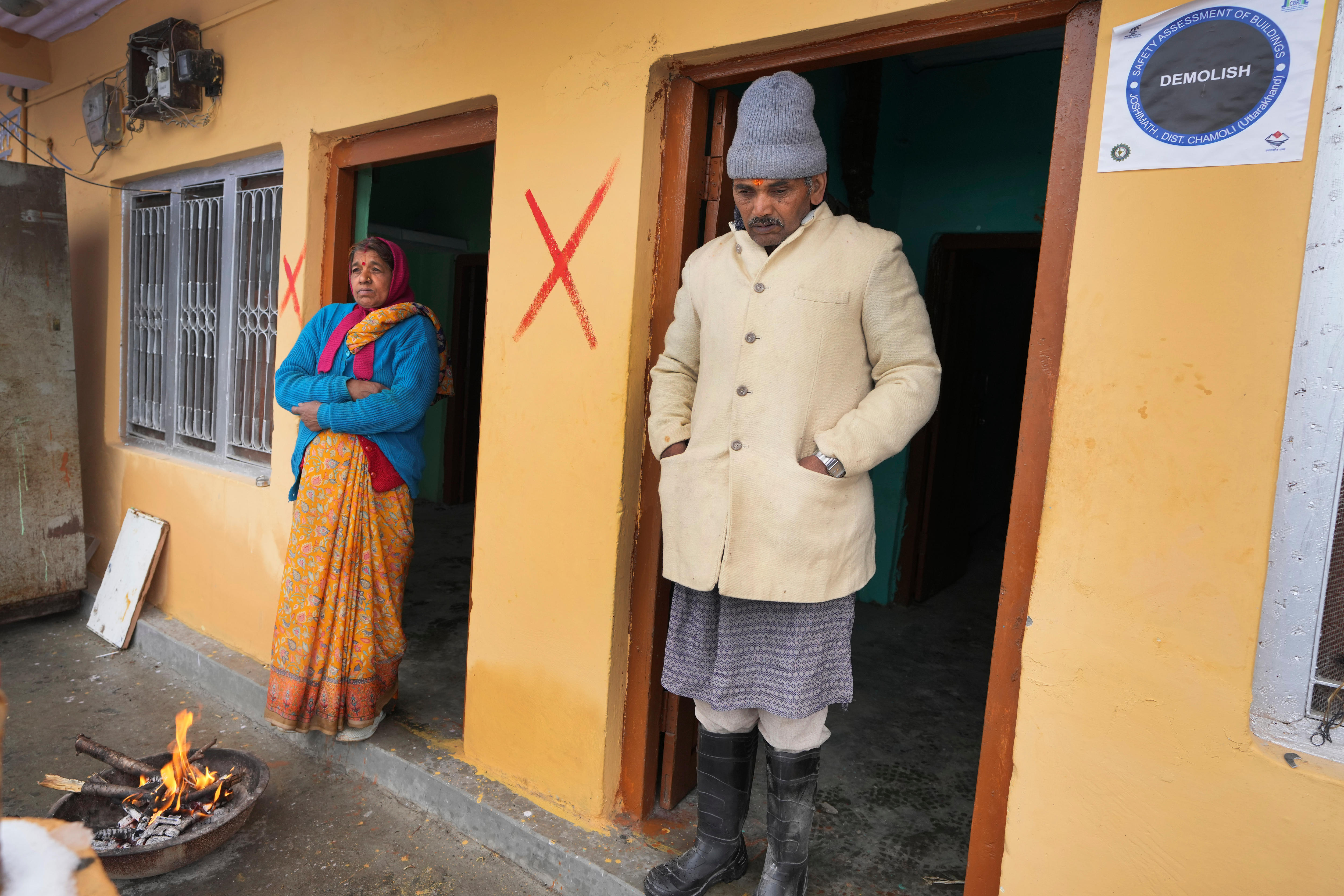A man and a woman stand in two doorways next to two red crosses on an orange wall. 