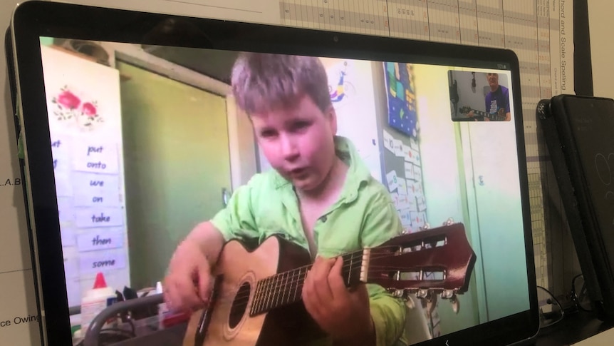 Young boy wearing light green shirt on a computer screen holds a guitar.