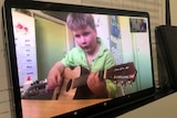 Young boy wearing light green shirt on a computer screen holds a guitar.