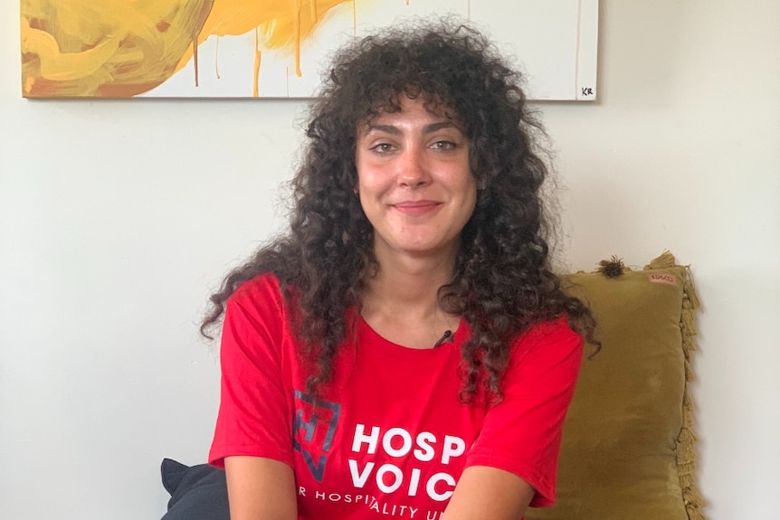 Hospitality worker Yasmine Sharaf sitting down wearing a red "Hospo Voice" shirt.