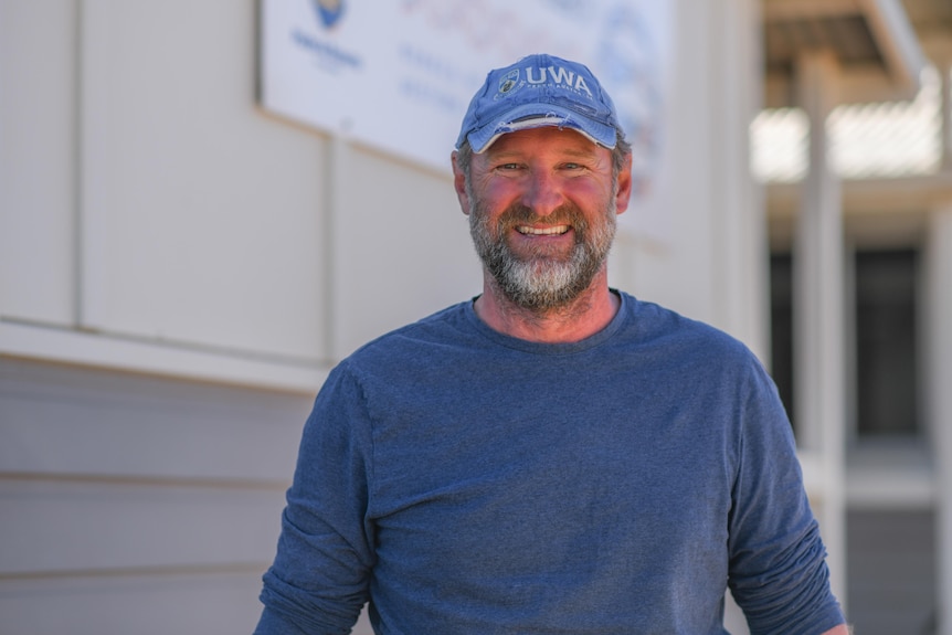 A man in a blue top and blue hat with a grey beard smiles