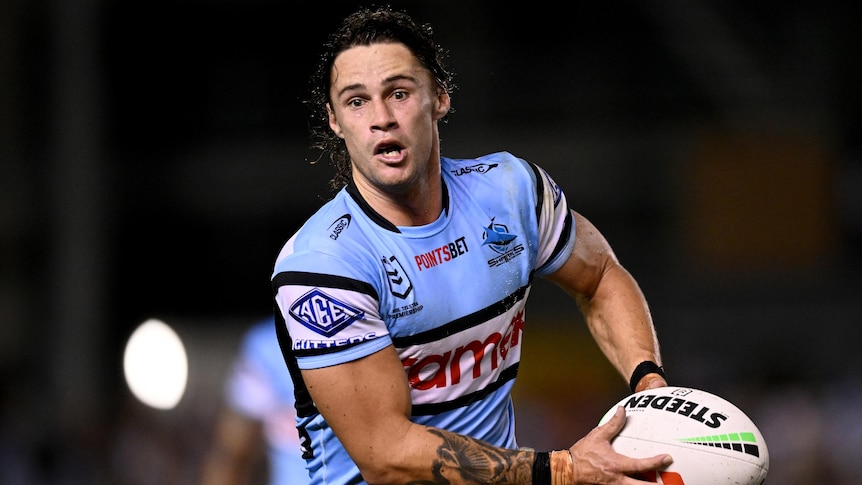 A Cronulla Sharks NRL player holds the ball in two hands during a match against North Queensland Cowboys.
