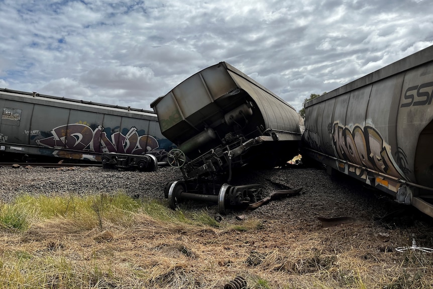 Train carriages lay scattered next to a rail line in the countryside.
