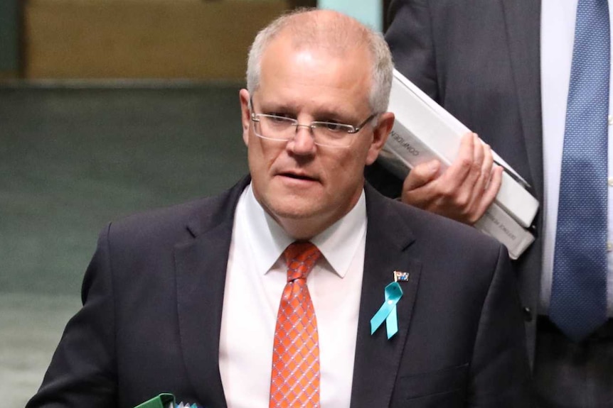 Mr Morrison has a bundle of folders under his arm, and is walking down the central aisle of the House of Representatives.