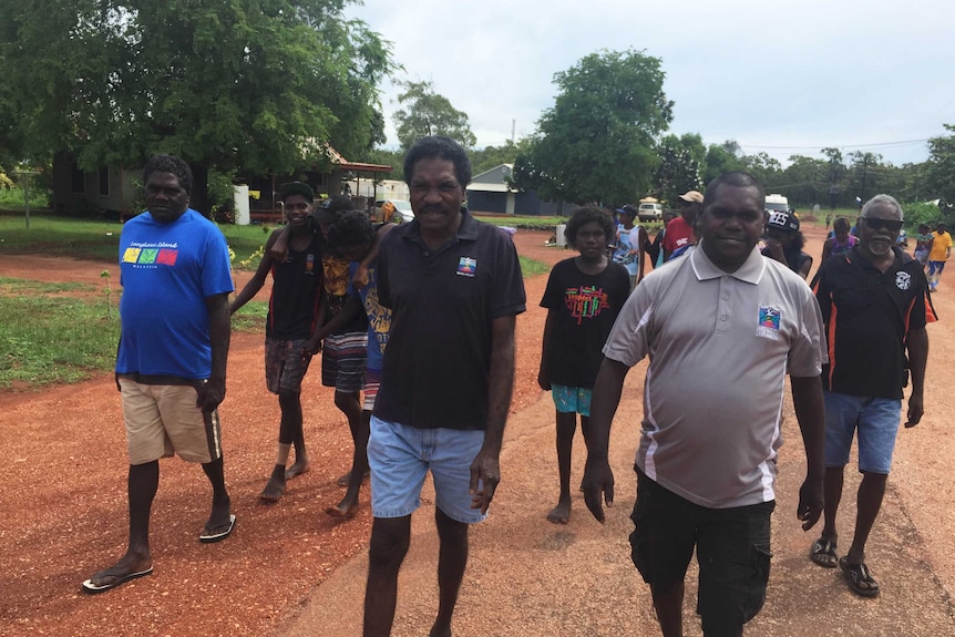 Two men walk in front of a large group of people in a remote Northern Territory community.
