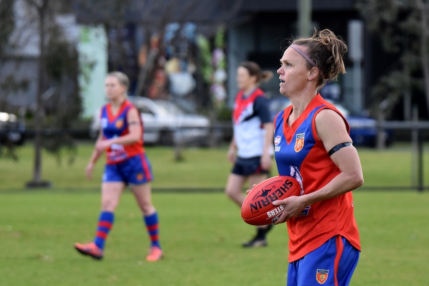 A female Aussie Rules player holds the ball in her hands as she prepares for a free kick.