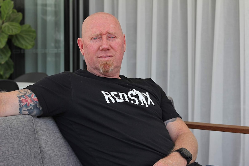 A man with an army tattoo and veterans support group t-shirt sits in a chair