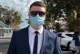 A man wearing a suit and tie with sunglasses and a covid face mask
