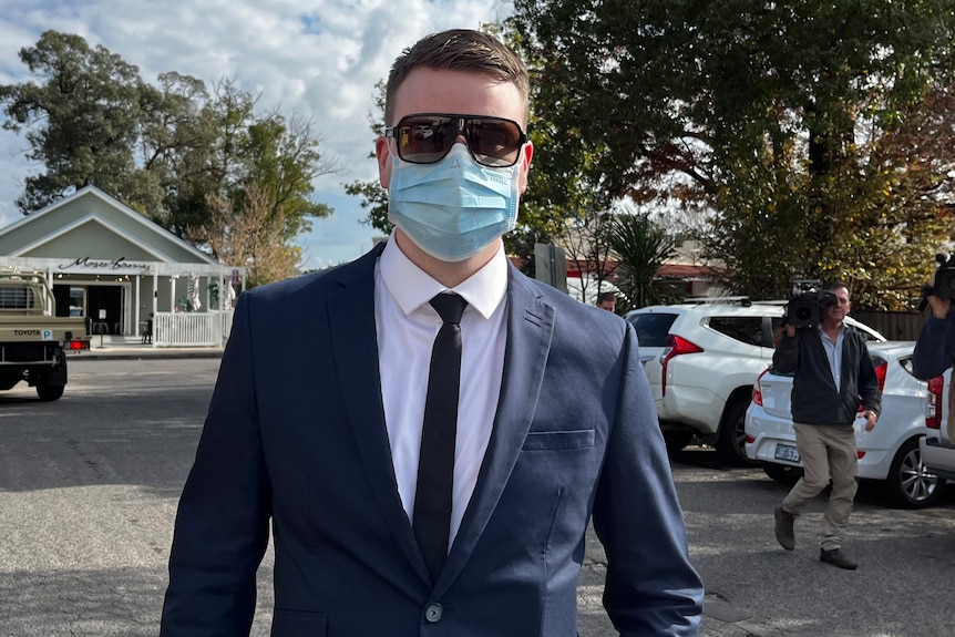 A man wearing a suit and tie with sunglasses and a covid face mask