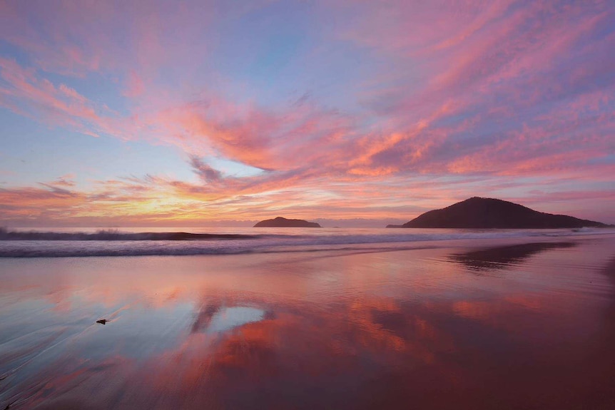 Light pink clouds reflected off of the ocean with islands  in the background