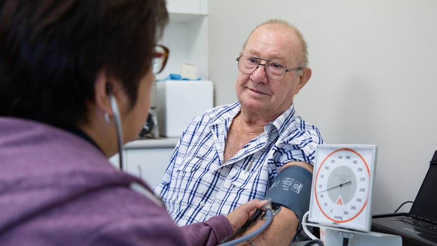 An older man receives a blood pressure check from a nurse.