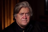 Headshot of Steve Bannon, showing him in a dark room, looking directly at the camera with a neutral expression