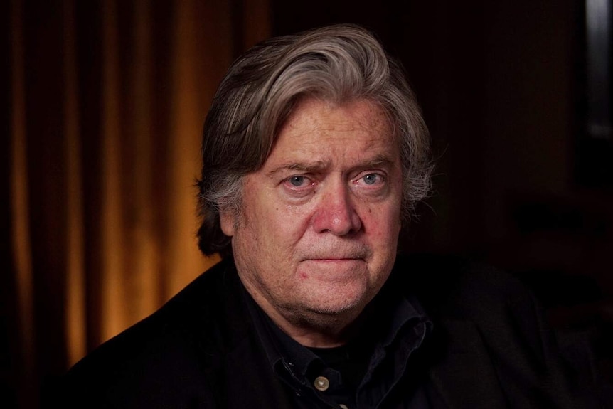 Headshot of Steve Bannon, showing him in a dark room, looking directly at the camera with a neutral expression